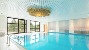 Una amplia piscina interior con agua cristalina azul, un diseño de techo moderno y grandes ventanales que ofrecen vistas al exterior.