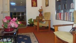 Uma sala de estar com estante, uma cadeira, uma mesa com um vaso de flores e um tapete.