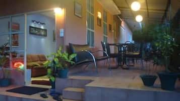 A covered outdoor seating area with a sofa, chairs, and potted plants.