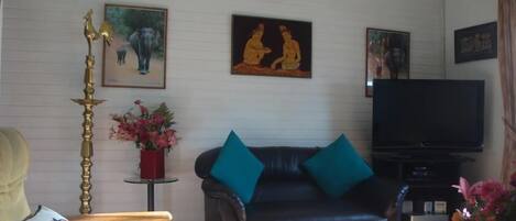 A living room with a leather sofa, teal cushions, a television, and framed artwork on the wall.