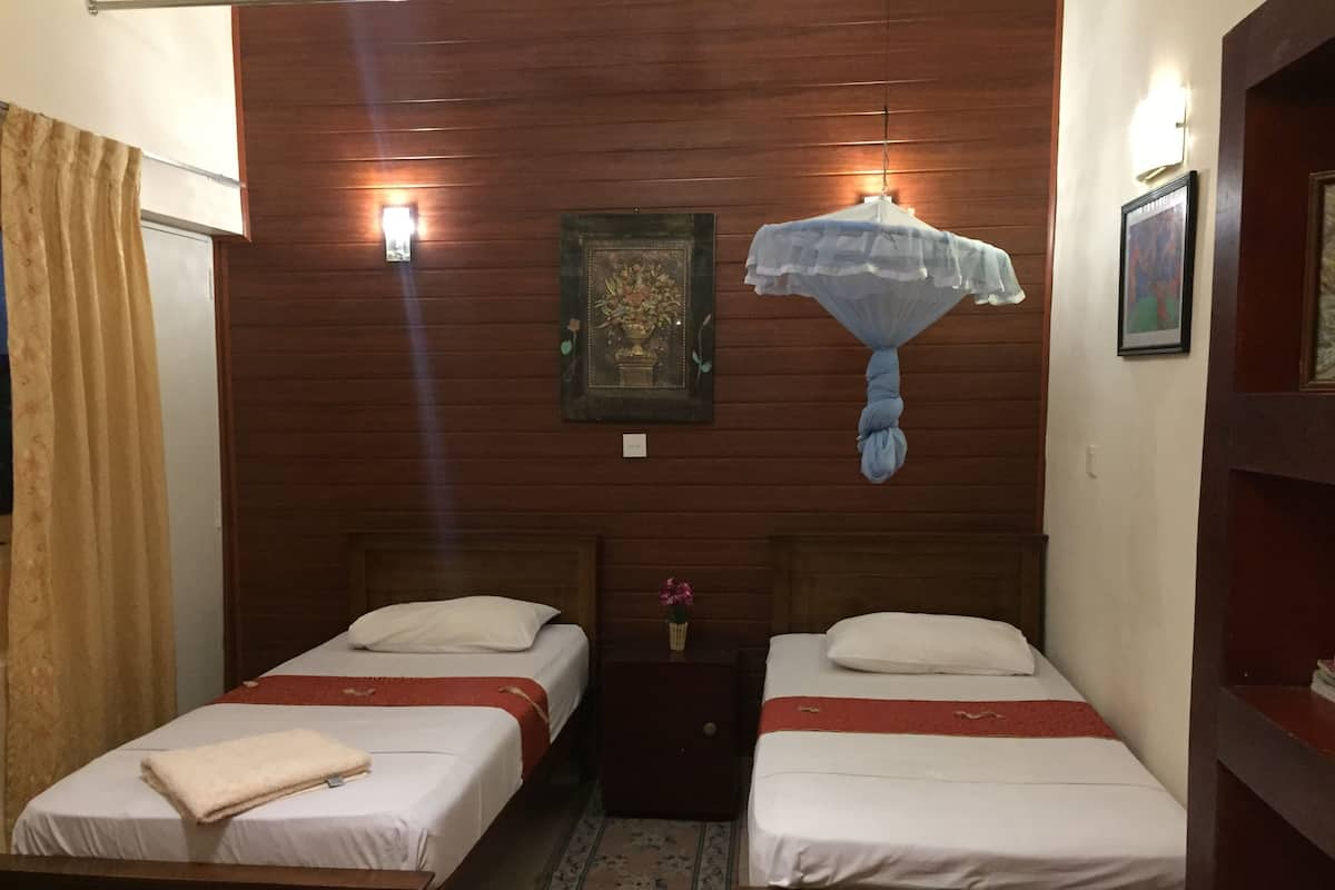 A room with two wooden beds, each with white bedding and a red stripe. There are wall-mounted lights, a framed picture, and a hanging light fixture.