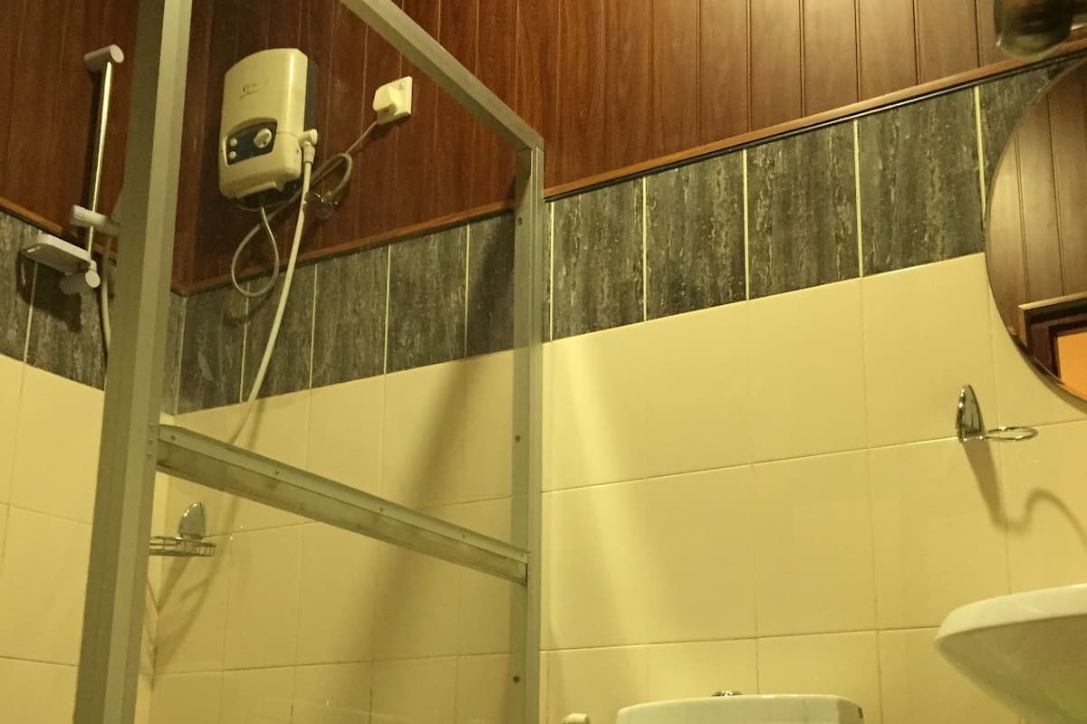 A bathroom with a toilet, a green trash bin, a shower area, and a sink.