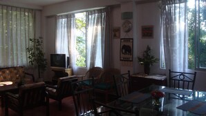 Uma sala de estar com sofá, cadeiras, televisão, mesa de jantar e cortinas.