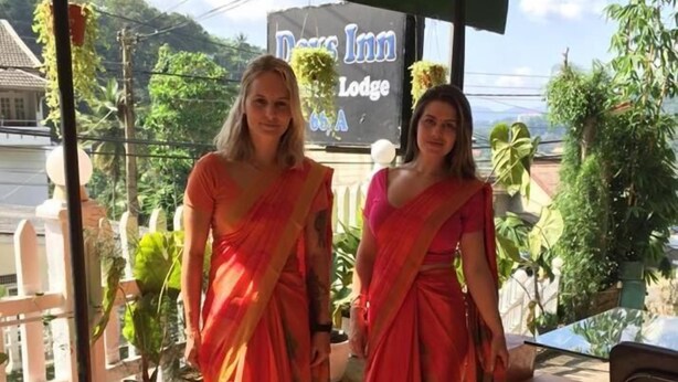Duas pessoas vestindo trajes tradicionais em uma área externa coberta, com uma placa indicando "Days Inn Lodge" ao fundo.