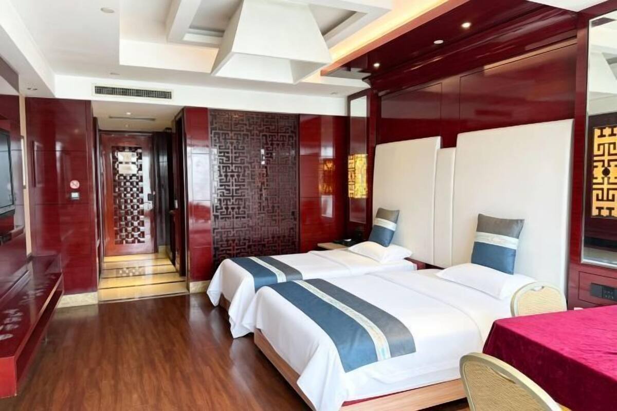 Habitación de hotel con dos camas, televisión, pared roja y suelo de madera.