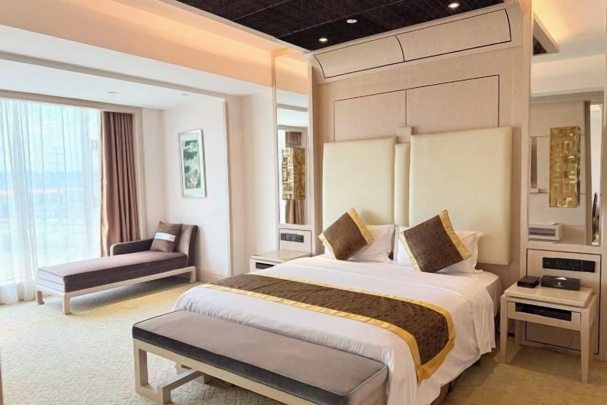 Une chambre d’hôtel avec un grand lit, une table de chevet, un banc et une vue sur l’extérieur.