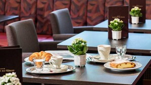 Una mesa de comedor preparada con platos, un croissant, un vaso de agua, una taza y una pequeña planta en maceta.