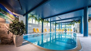 Una piscina interior con sillas amarillas, una maceta grande de piedra y un techo azul.