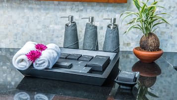 A bathroom with a black sink, three towel dispensers, a potted plant, and rolled towels with flowers.