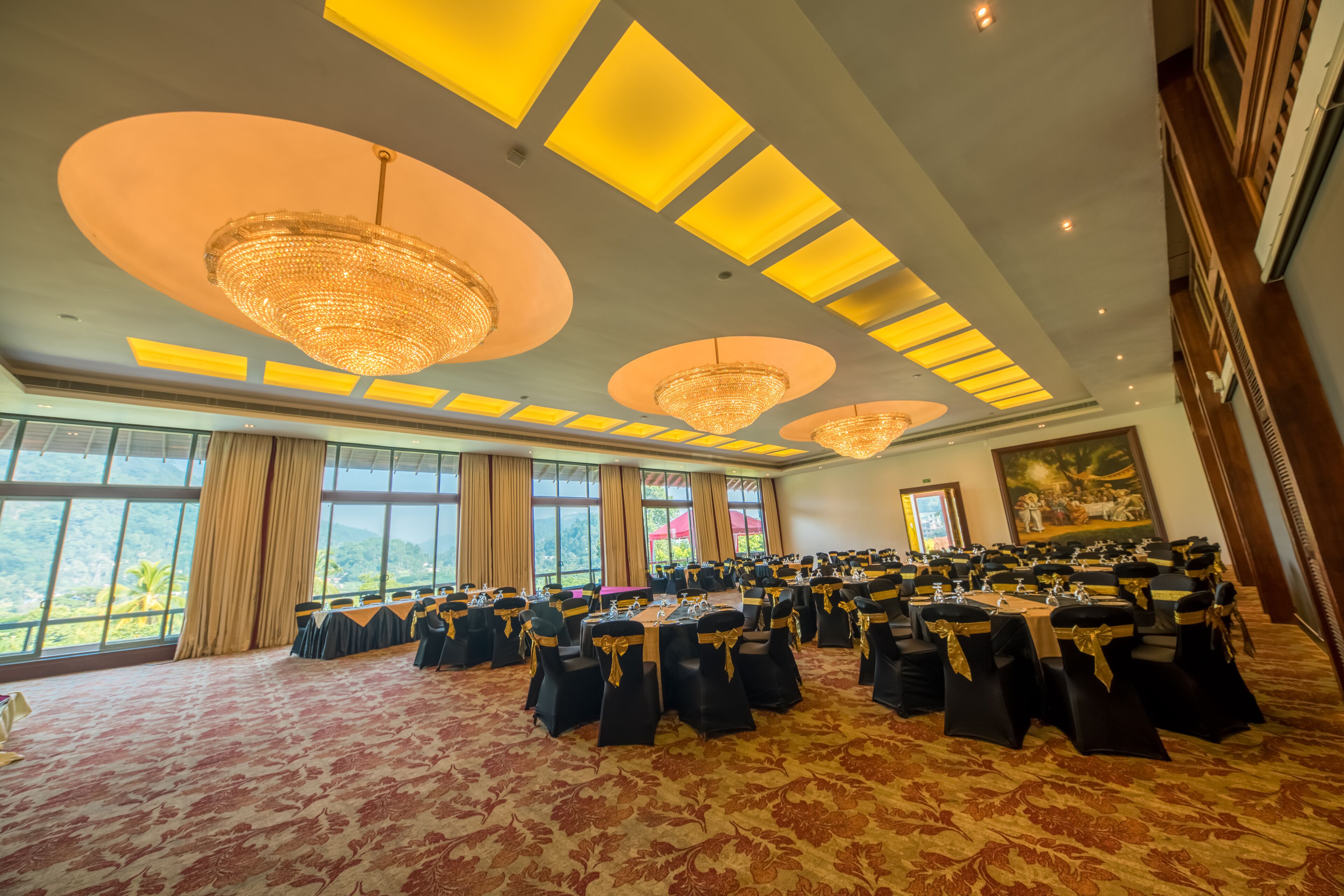 A large conference room with round tables, black chairs with gold sashes, and a chandelier.