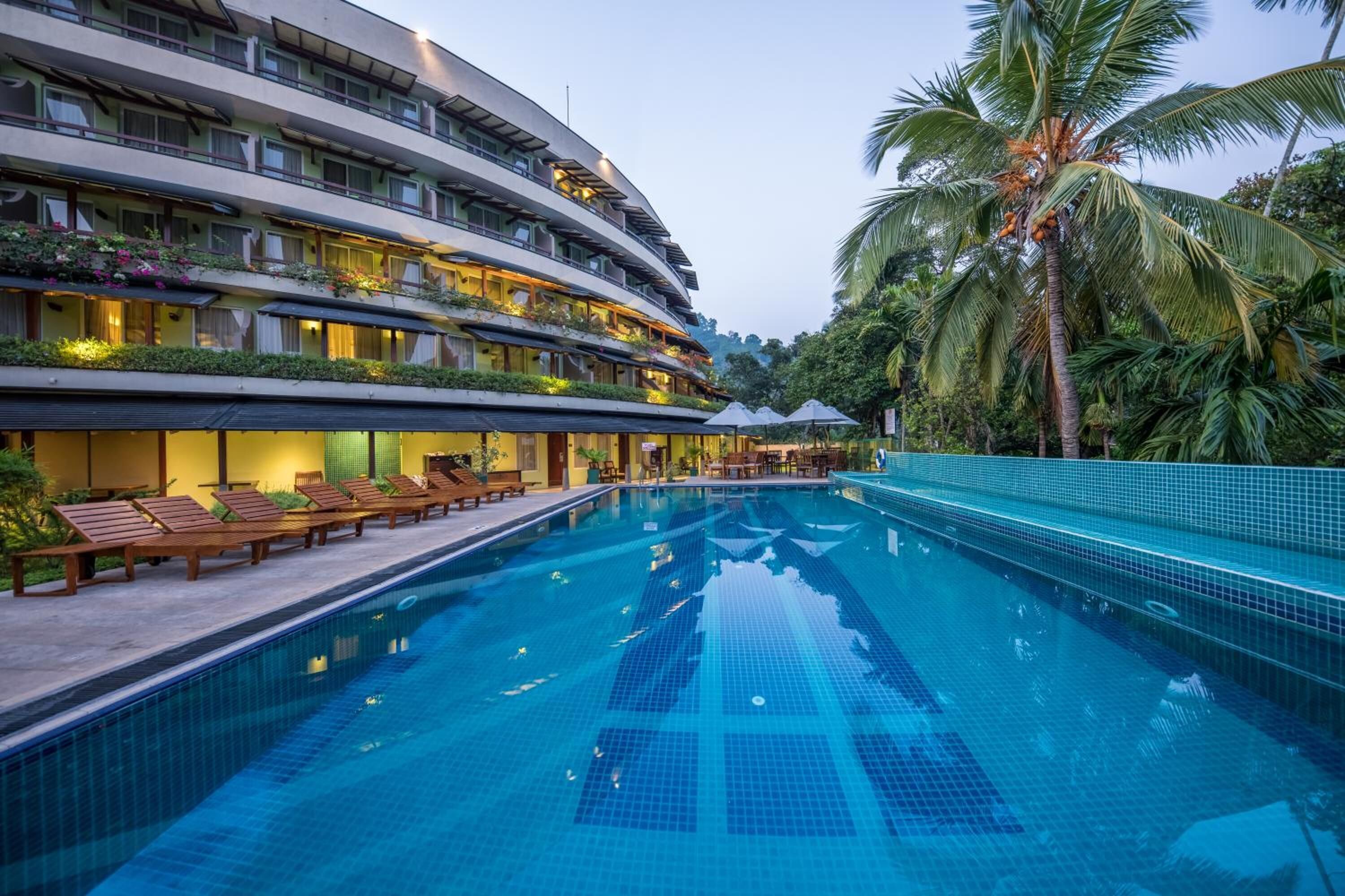 Een hotel met een zwembad, meerdere balkons met beplanting, en een palmboom.