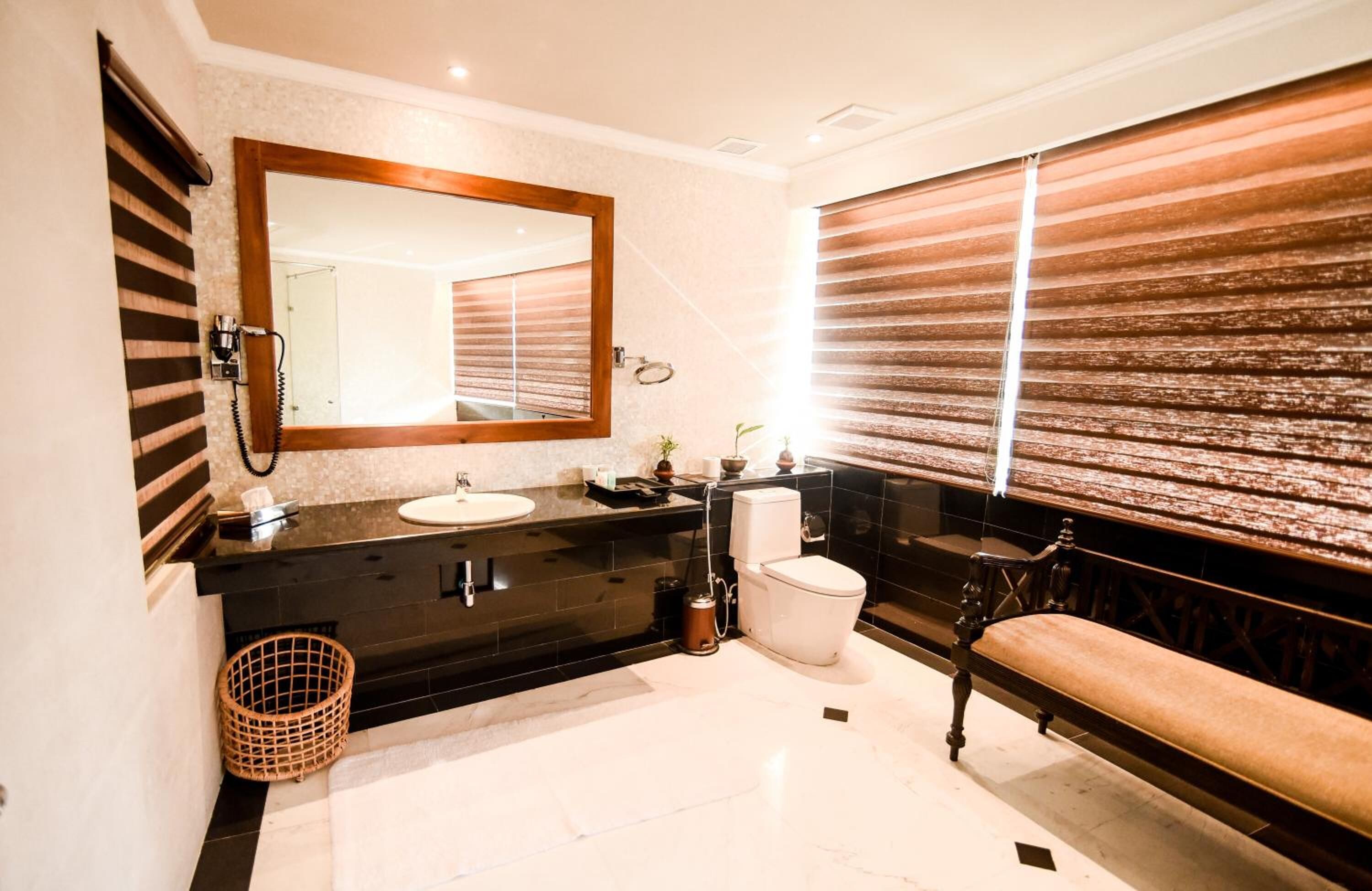 A modern bathroom with a large mirror, a sink, a toilet, and a bench.