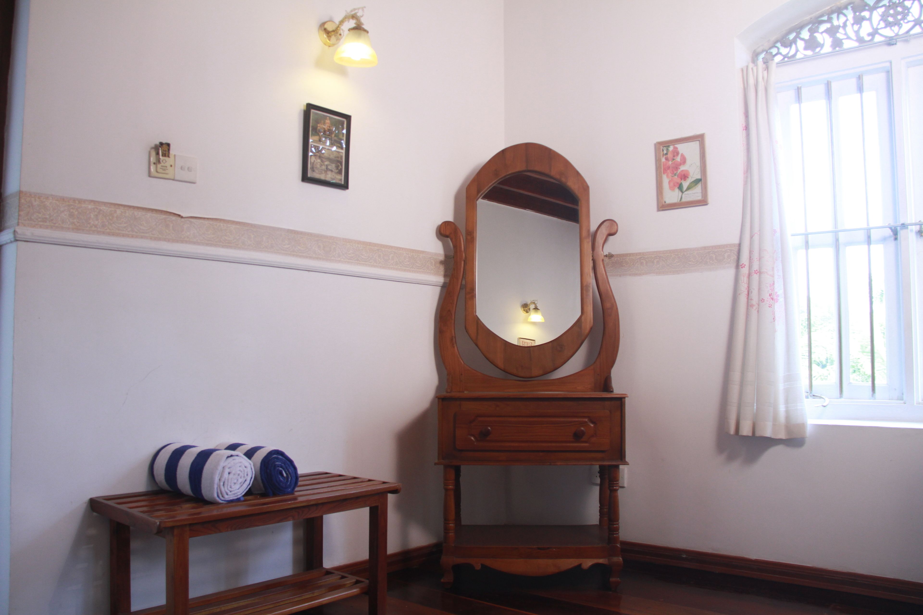 A wooden dresser with a mirror, a small table with towels, and a window with a curtain.