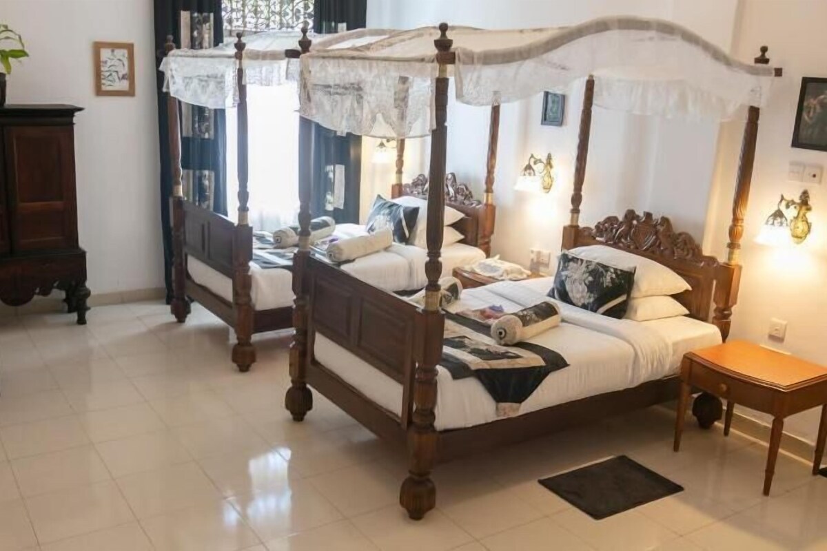 A four-poster bed with a canopy, a wooden cabinet, a round table with chairs, and a small bedside table.