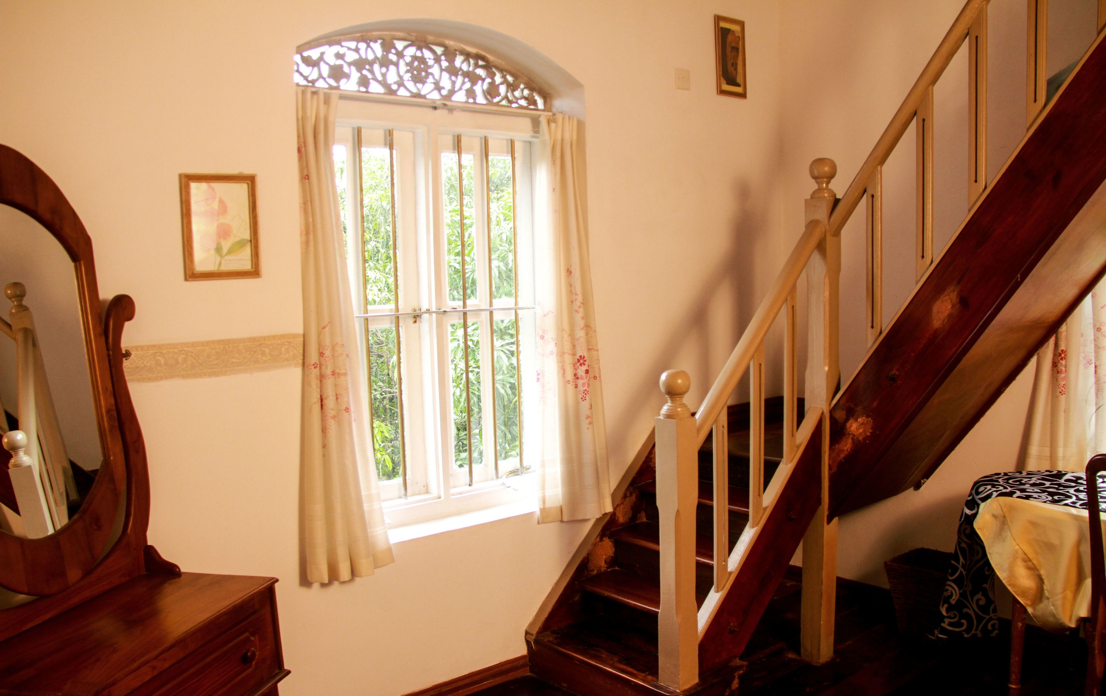 Una escalera con barandillas y pasamanos de madera que lleva a un rellano con una ventana y un espejo.
