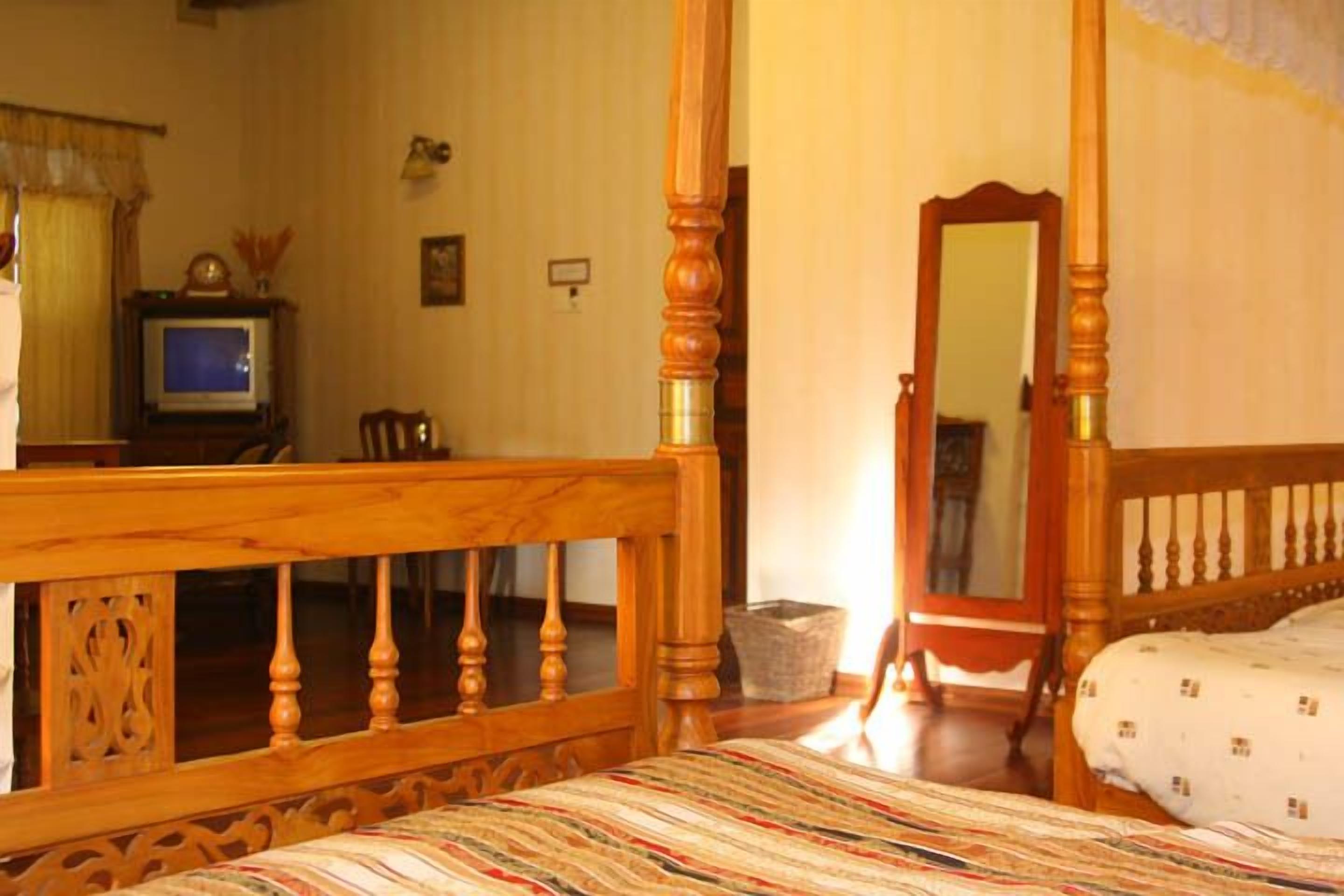 A bedroom with a wooden four-poster bed, a television, and a mirror.