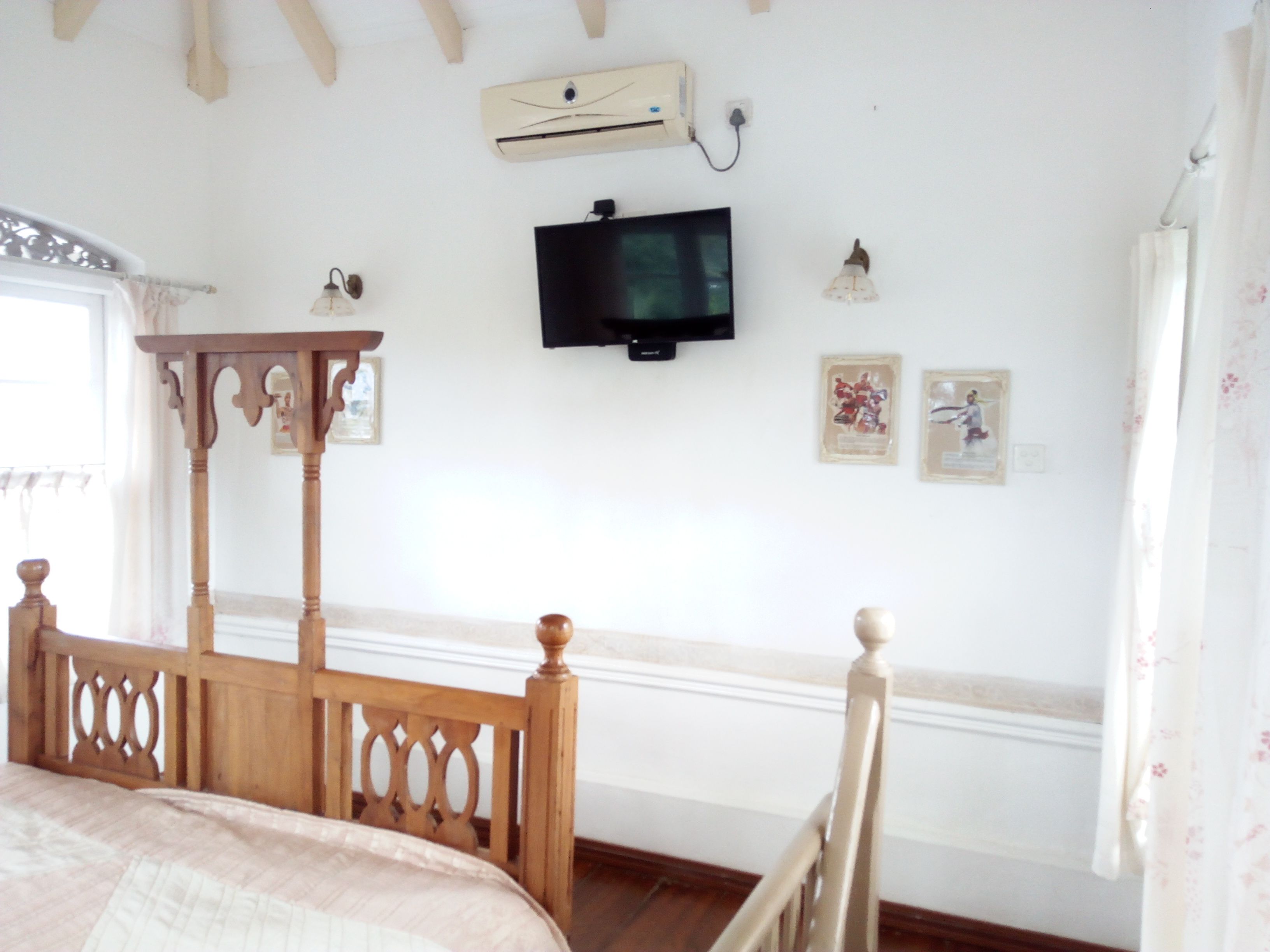 A bedroom with a wooden four-poster bed, a television mounted on the wall, and a small table.