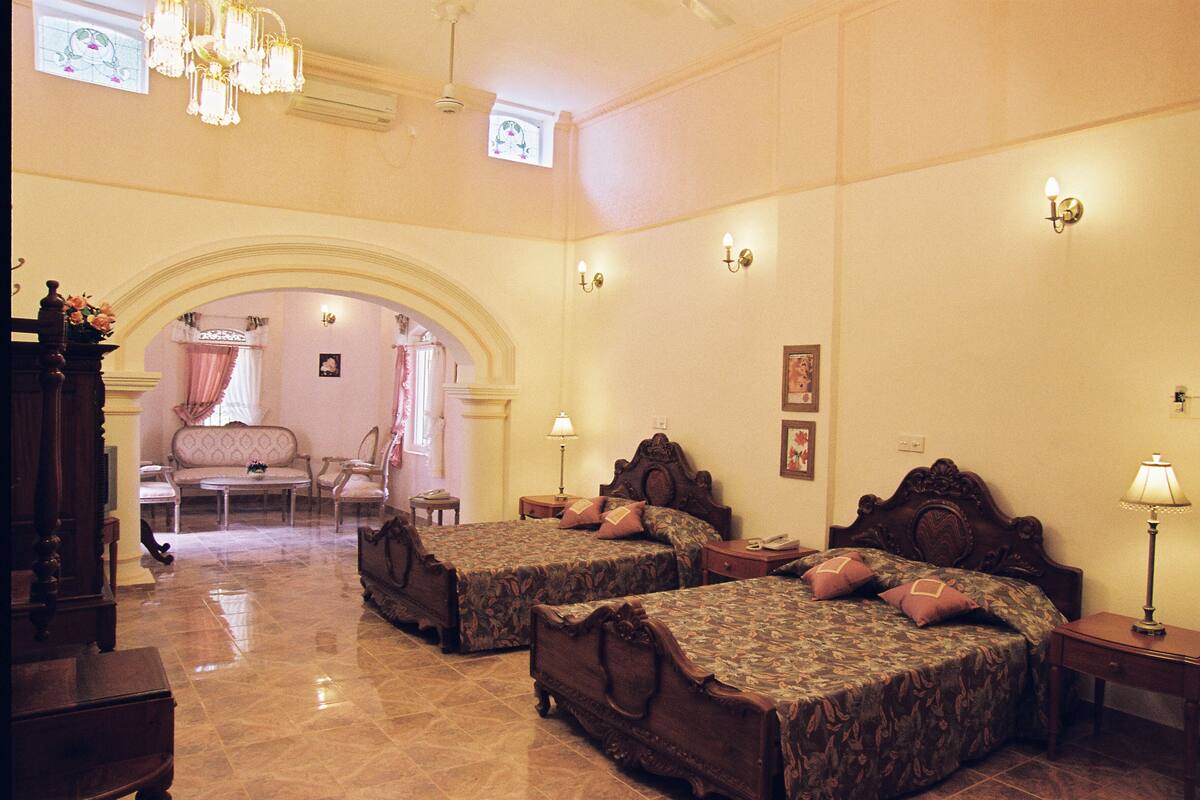 A hotel room with two beds, a sitting area with a sofa and chairs, and a chandelier.