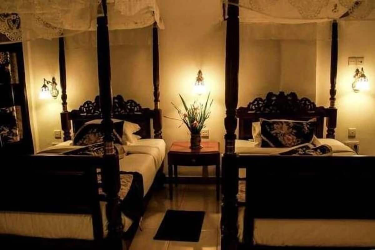 A dimly lit room with four wooden beds arranged in a square, each with a nightstand and a lamp.