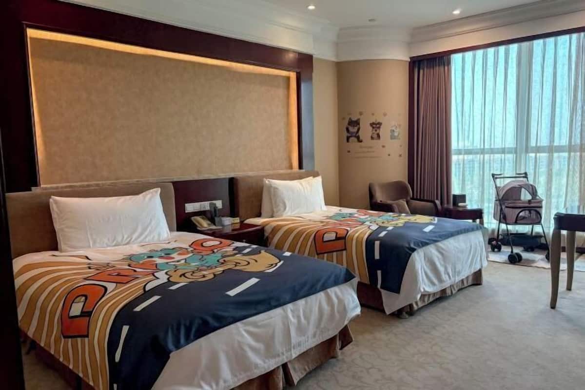 A hotel room with two beds, a desk, a chair, and a large window.