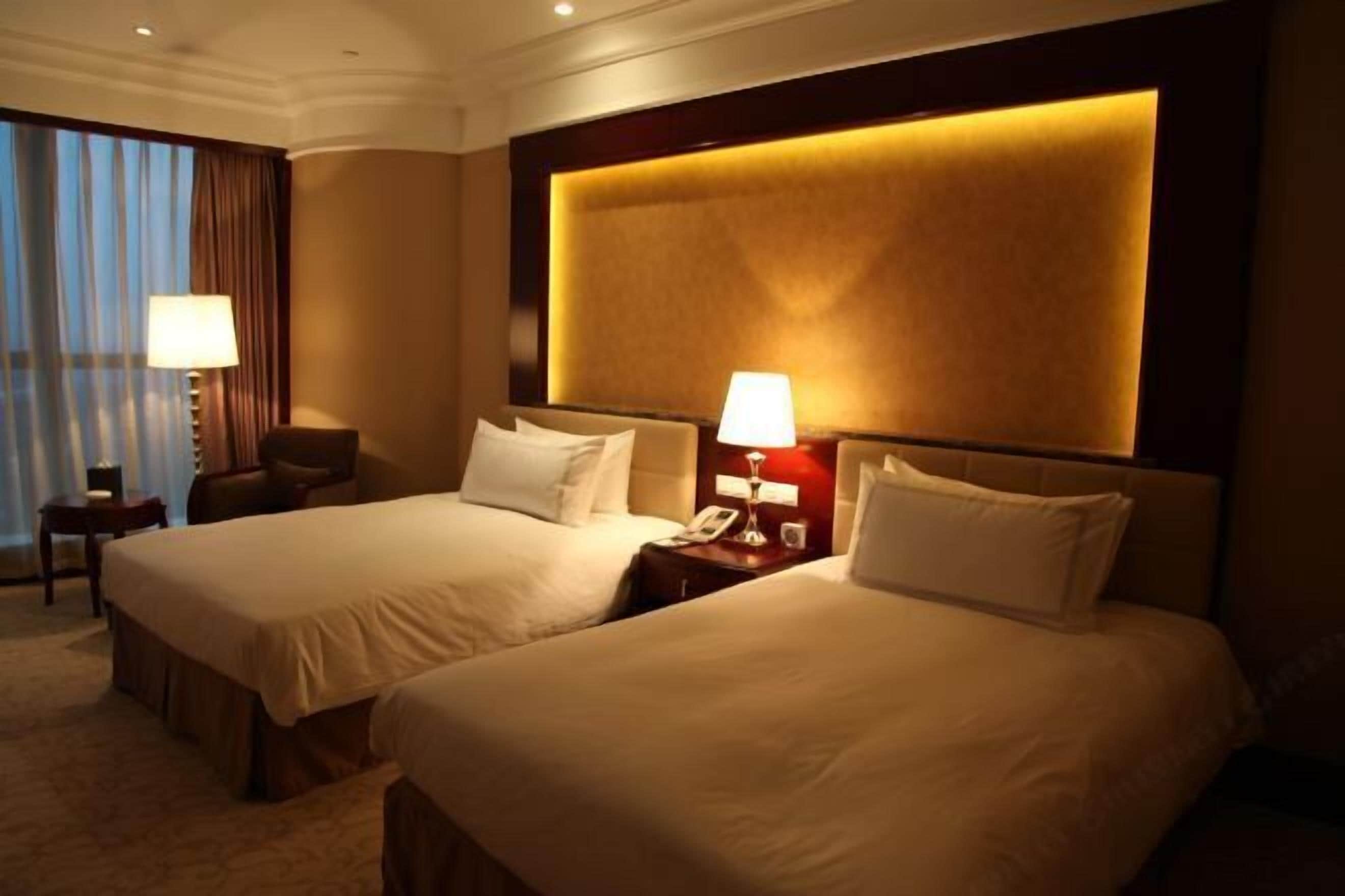 Een hotelkamer met twee bedden, een nachtkastje met lamp, een telefoon en een raam met gordijnen.