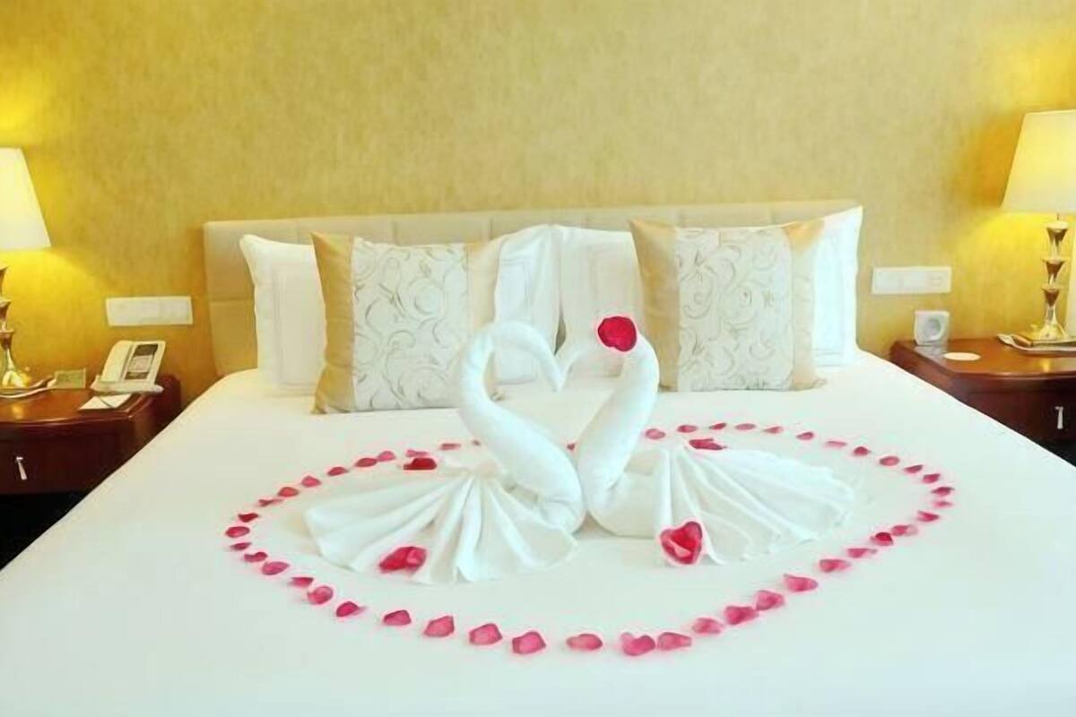 A hotel room with a bed, pillows, a nightstand, a lamp, and a wall clock.