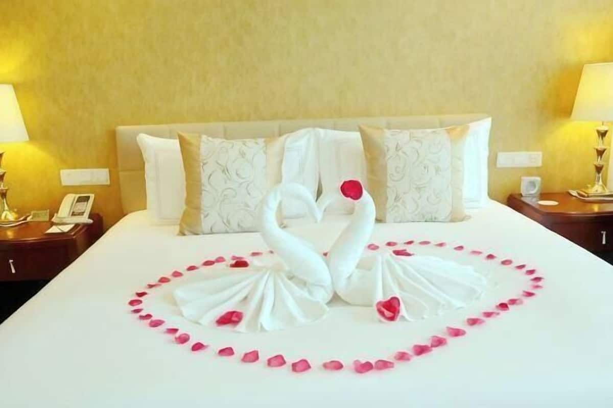 A hotel room with a bed, pillows, a nightstand, a lamp, and a wall clock.
