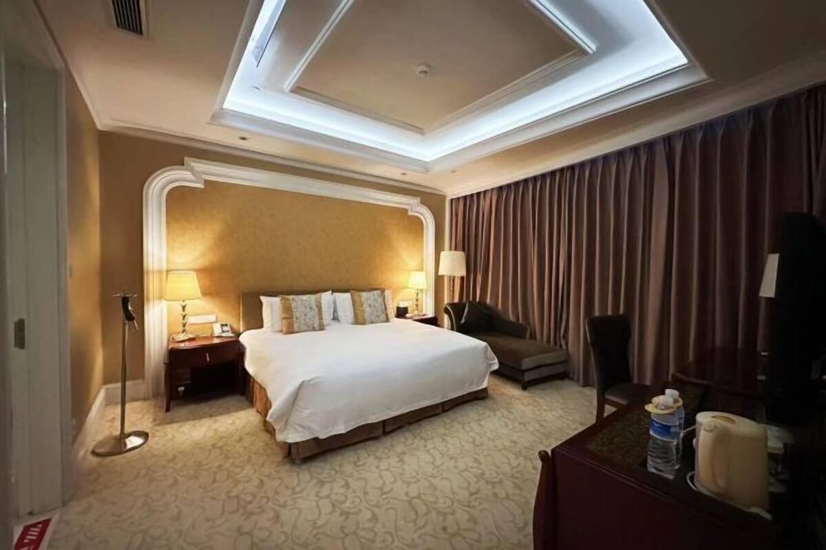 A hotel room with a large bed, a desk, a chair, a lamp, and a ceiling light fixture.