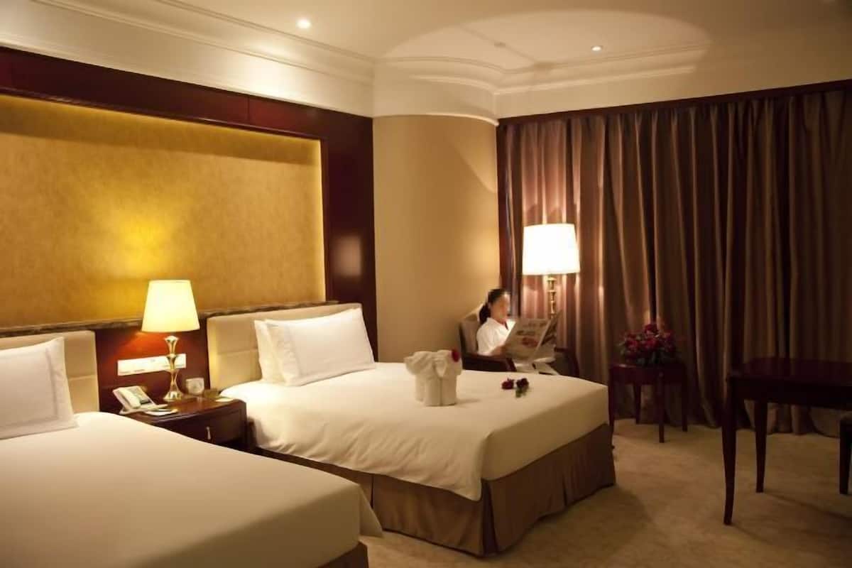 A hotel room with two beds, a desk, a chair, a lamp, and a curtain.