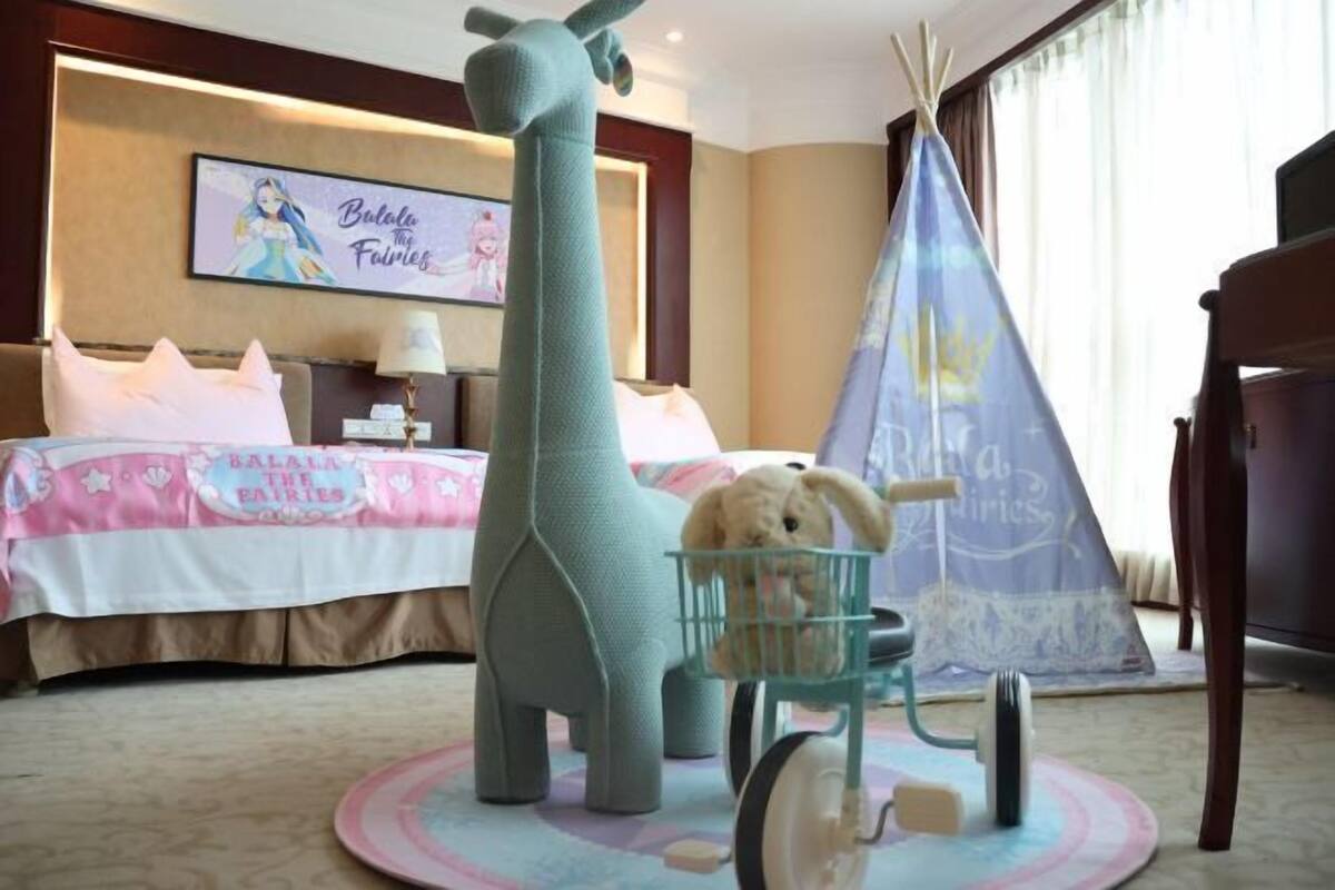 A hotel room with a bed, a large giraffe decoration, a small chair, and a teepee.