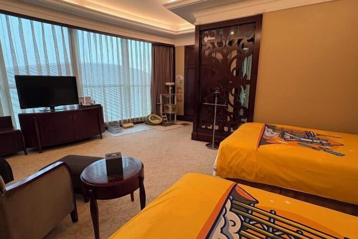 A hotel room with a bed, a TV, a desk, a chair, and a window with curtains.