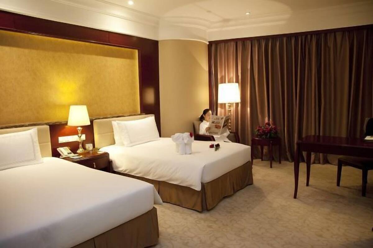 A hotel room with two beds, a desk, a chair, a lamp, and a curtain.