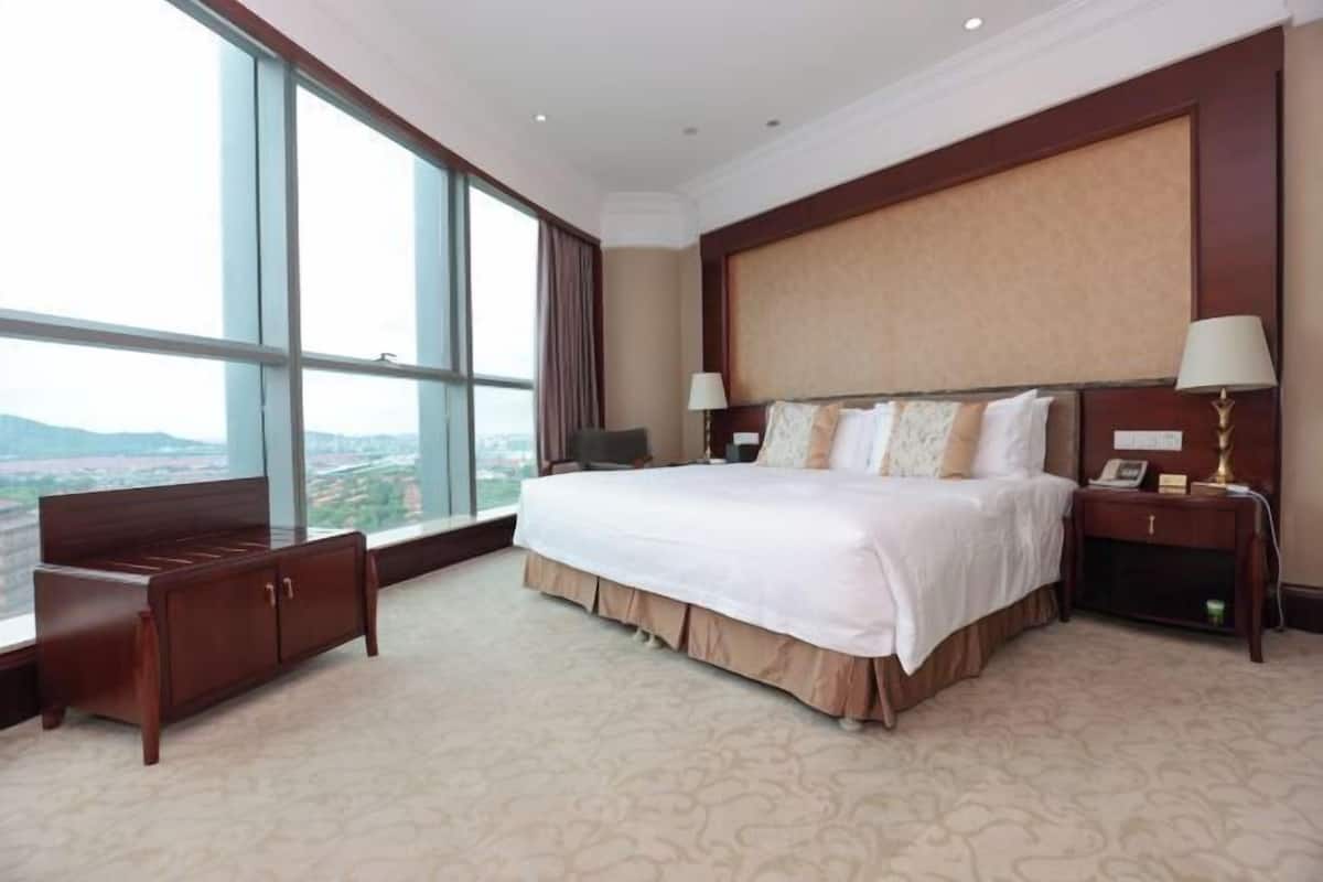A hotel room with a large bed, a desk, a chair, and a view of the city.