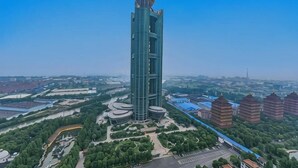 A tall, modern building with a unique dome structure, surrounded by greenery and other buildings. - Long Wish Hotel International (Jiangyin)