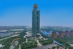 A tall, modern building with a unique dome structure, surrounded by greenery and other buildings. - Long Wish Hotel International (Jiangyin)