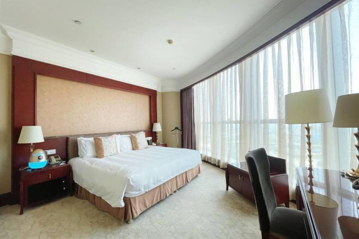 A hotel room with a large bed, a nightstand, a desk with a lamp, and a chair.