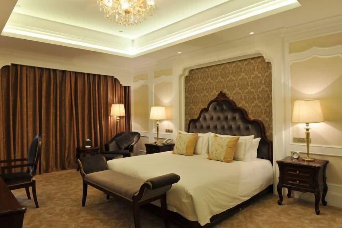 A hotel room with a large bed, two bedside tables, a chair, a desk, and a chandelier.