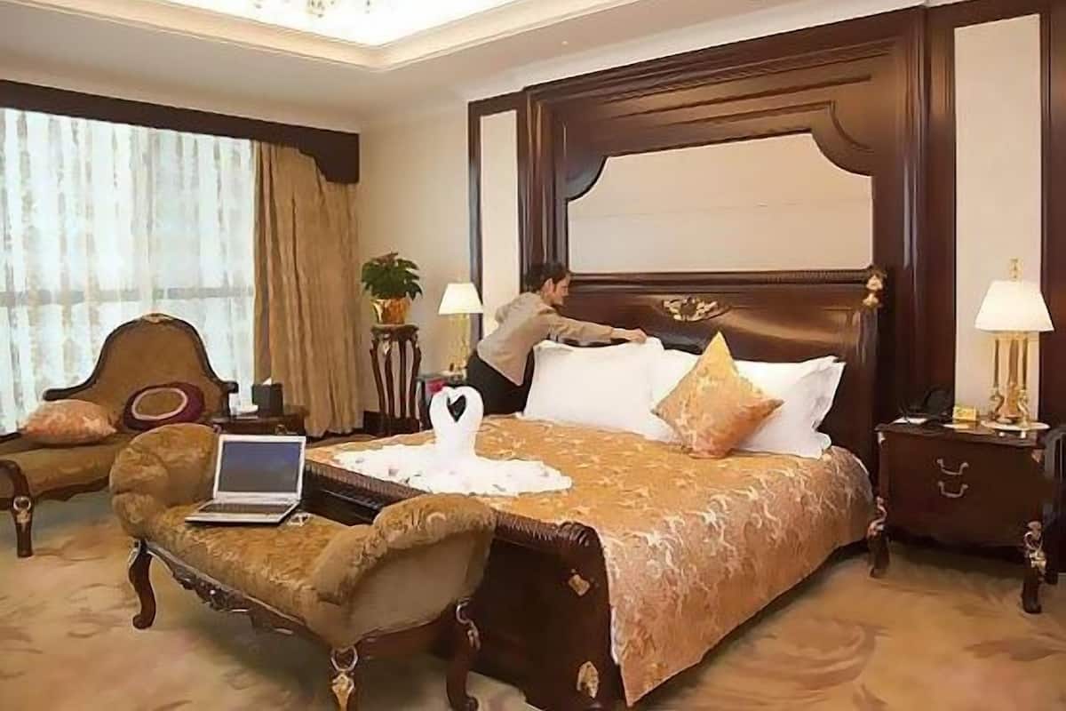 A hotel room with a large bed, a desk with a laptop, a chair, and a nightstand with a lamp.
