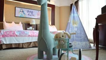 A hotel room with a large stuffed giraffe, a small toy cart, and a decorative teepee.