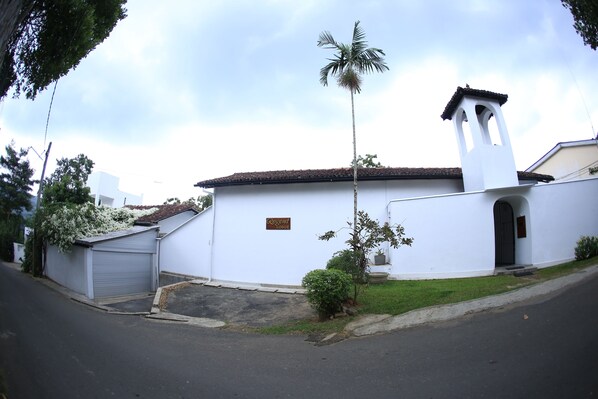 A white building with a bell tower, a garage, and a small garden area.