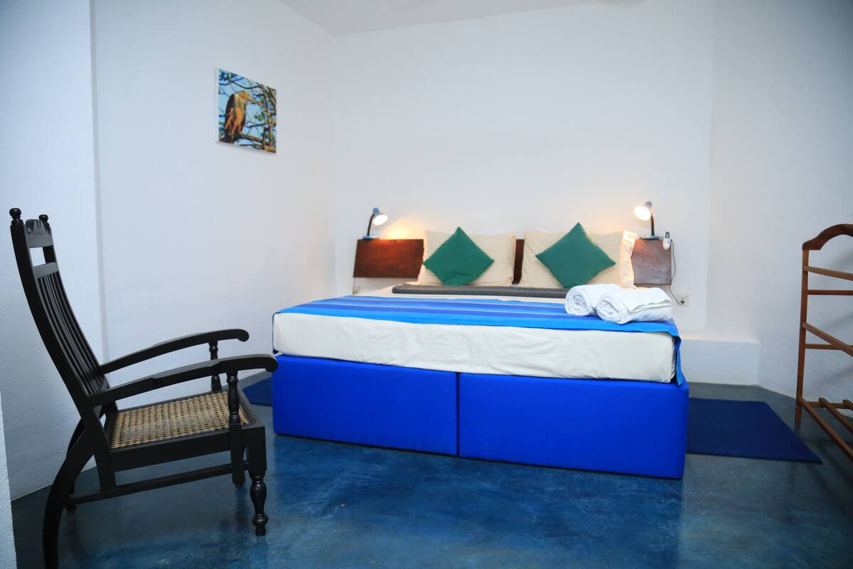 A bedroom with a bed, a chair, a painting, and bedside lamps.