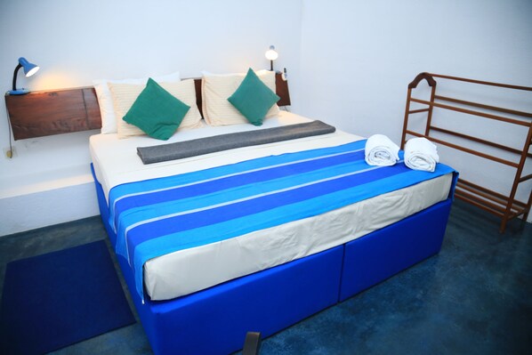 A neatly made bed with blue and white bedding, a wooden headboard, and two rolled towels on the footboard.