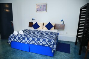A bedroom with a bed, pillows, a bedside table, a wall-mounted lamp, and a door.