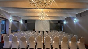 Une salle de conférence avec des rangées de chaises blanches, un grand lustre et un écran de projection.
