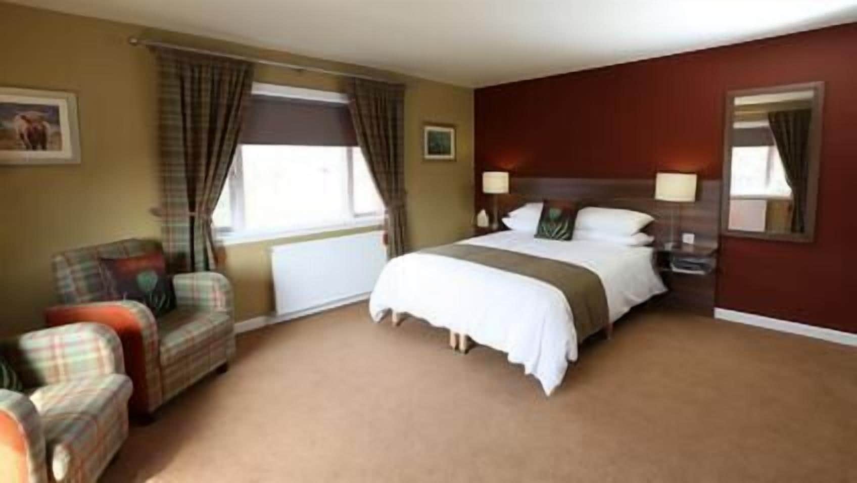 A hotel room with a bed, a chair, a nightstand, a lamp, and a window with curtains.