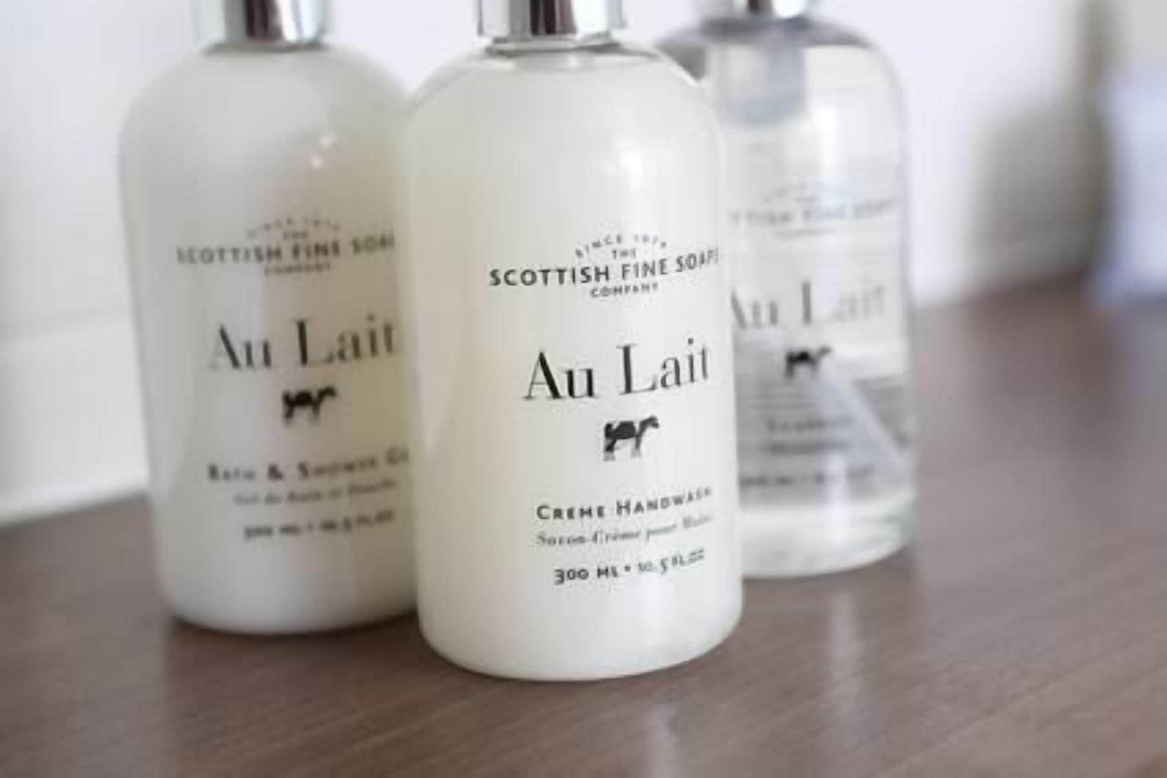 Three bottles of Au Lait Scottish Fine Soap on a wooden surface.