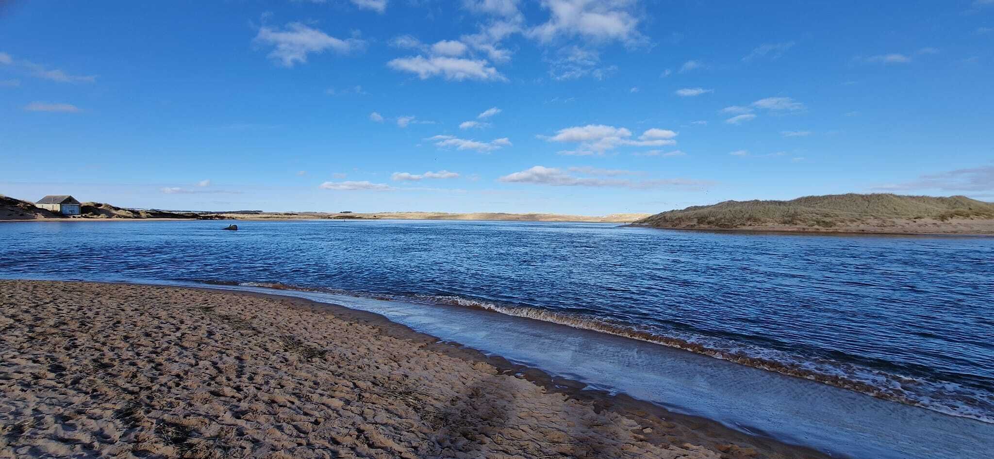 Una playa con agua azul cristalina, una orilla arenosa y colinas a lo lejos.