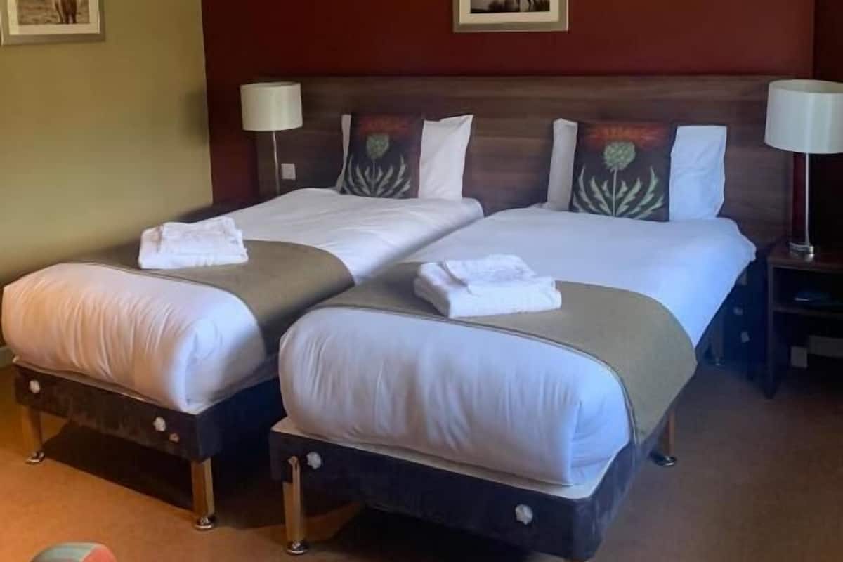 Ein Hotelzimmer mit zwei Einzelbetten, einem Holzkopfteil und einem Nachttisch mit Lampe.