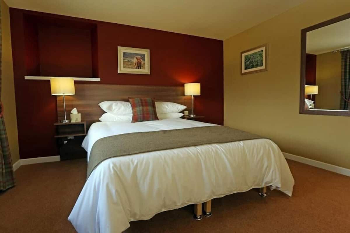 Ein Hotelzimmer mit einem großen Bett, zwei Nachttischen, einer Kopfteil und zwei Wandlampen.