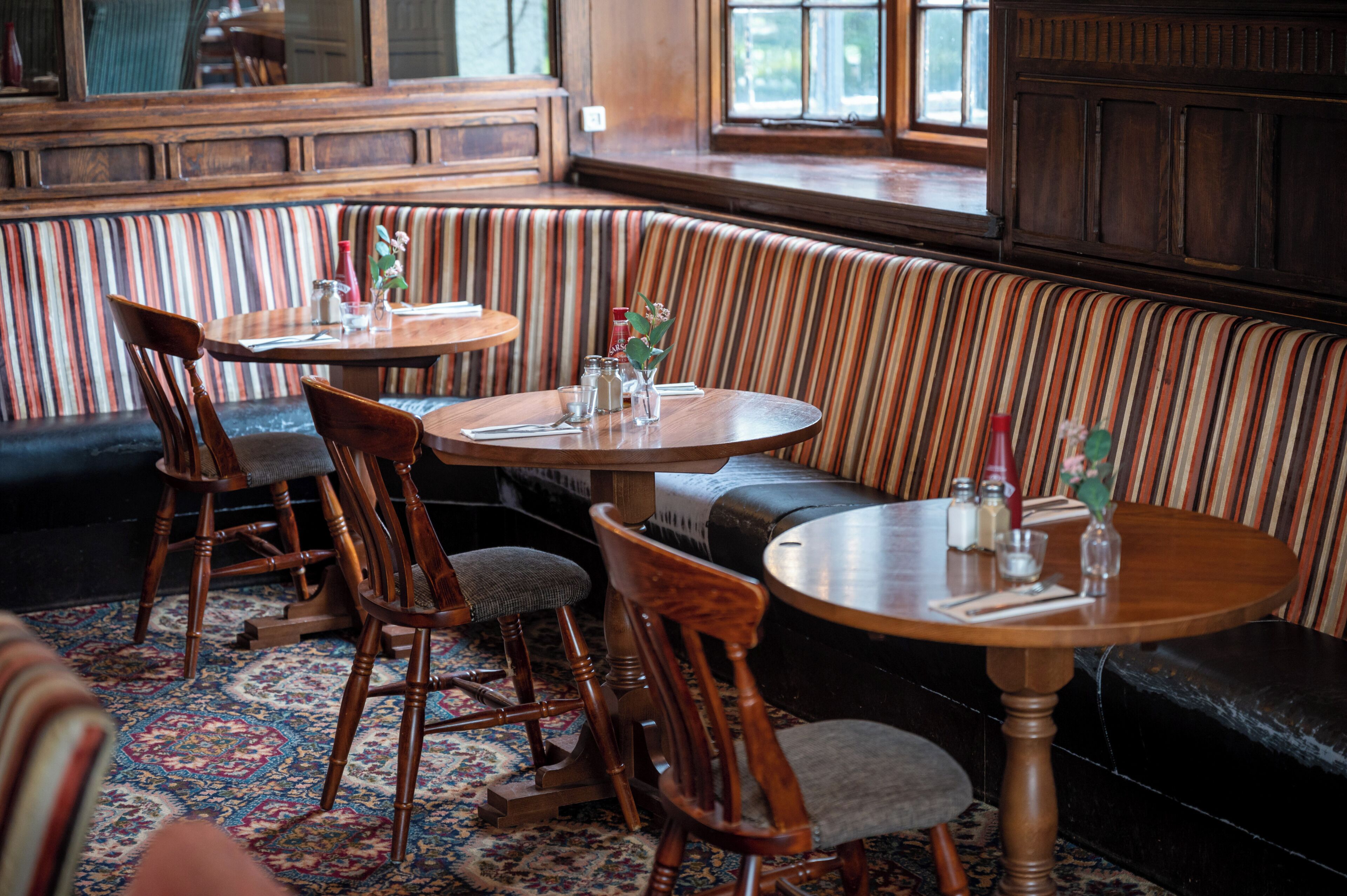 Ein gemütliches Restaurant-Interieur mit gestreifter Polsterung, Holztischen und einem gemusterten Teppich.